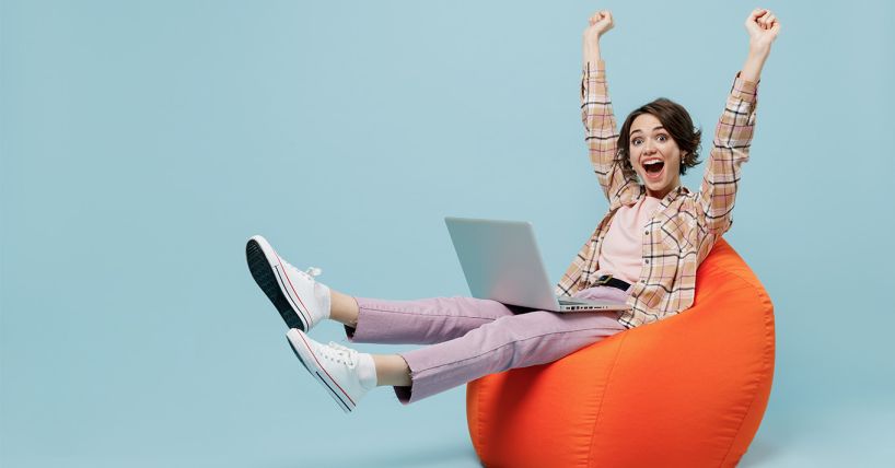 Excited woman in beanbag with her arms up in the air and a laptop on her lap.